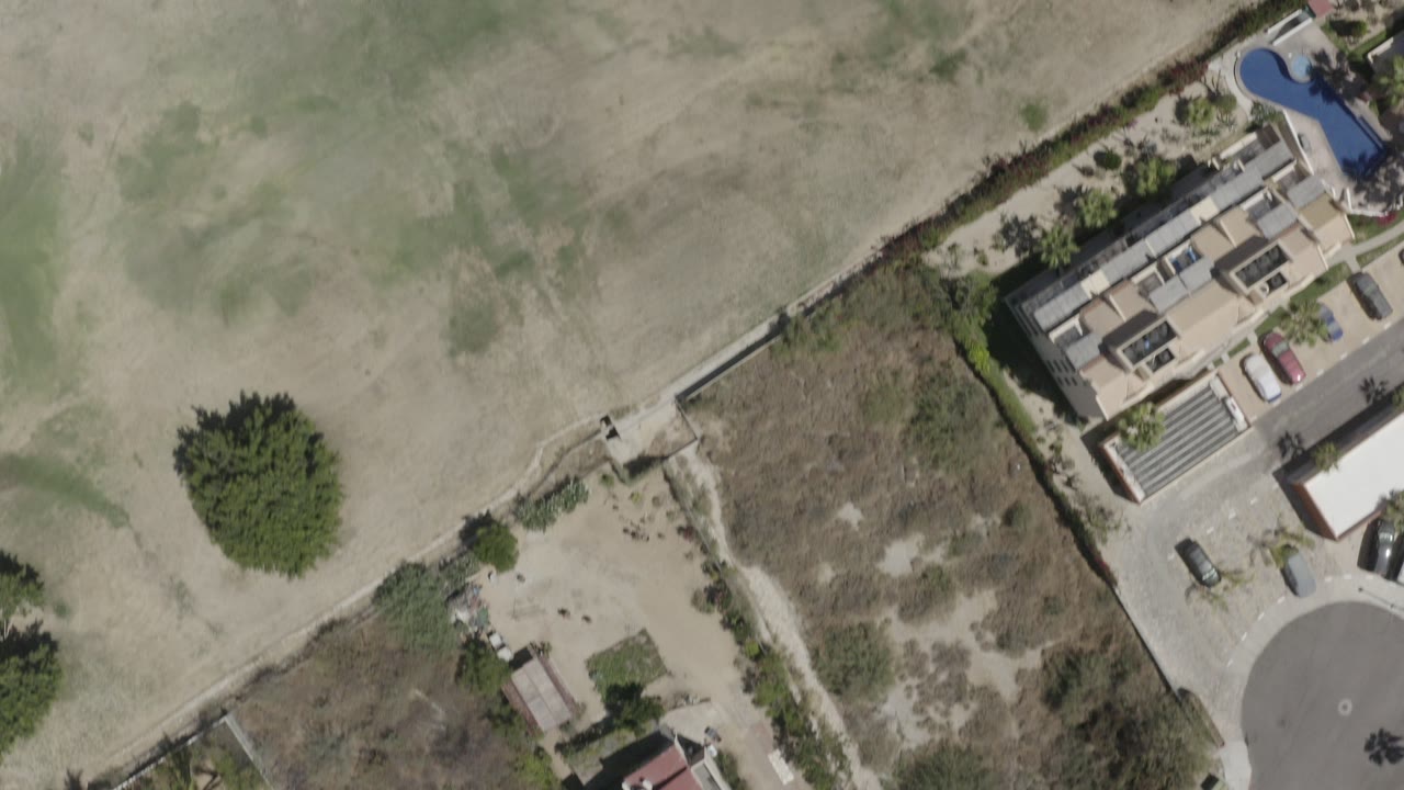 Top-down aerial view of lawns, a walled home, trees, and sandy paths.