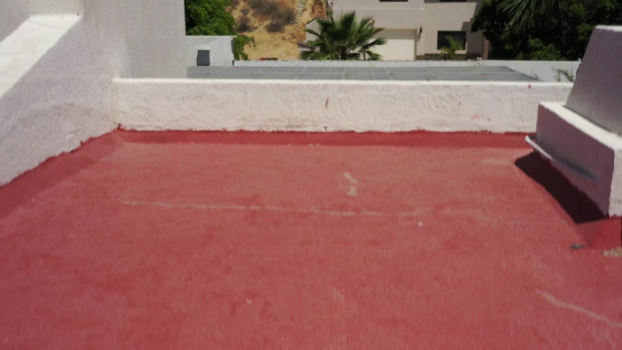 Red rooftop with white parapet and nearby buildings beyond