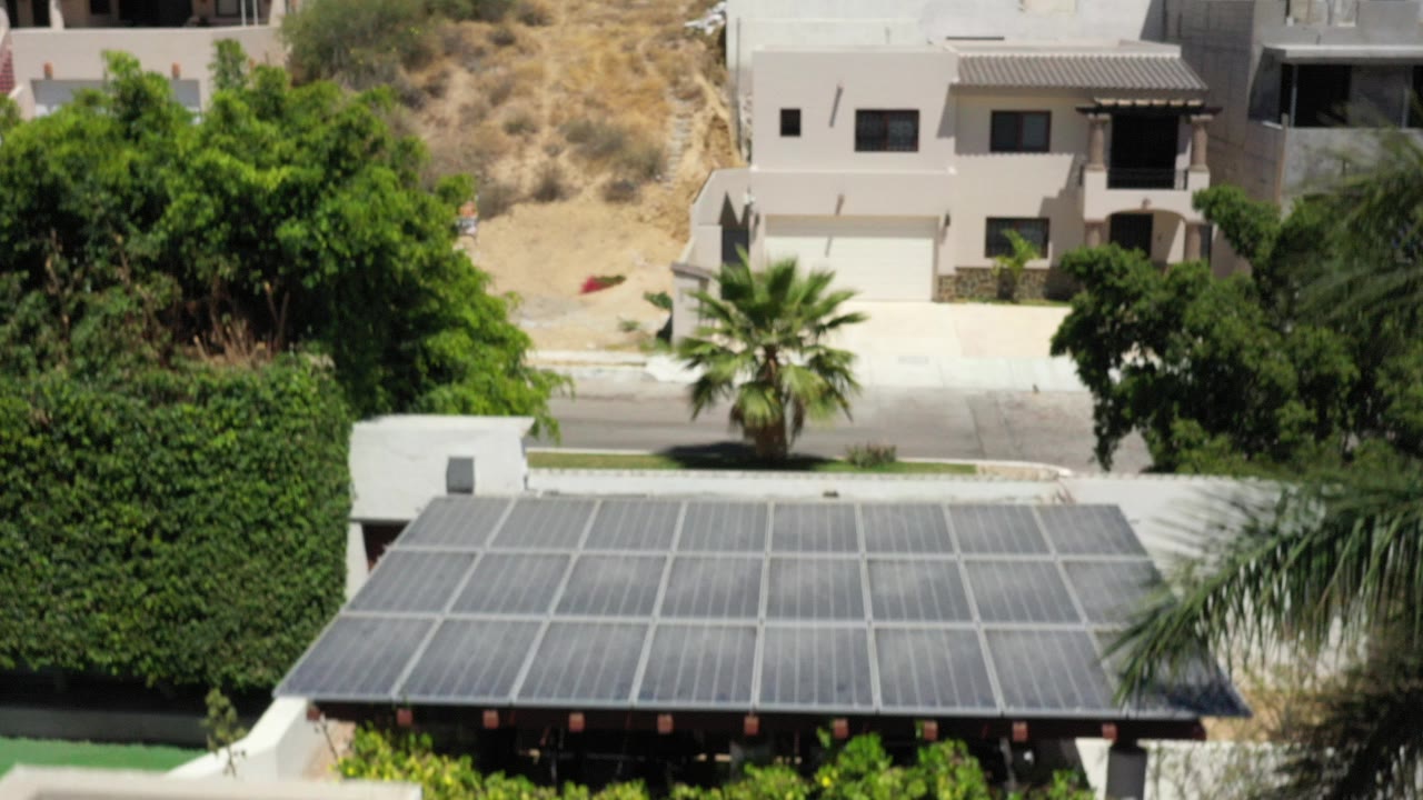 Aerial view of a solar-panel roof, trees, road, and modern homes.