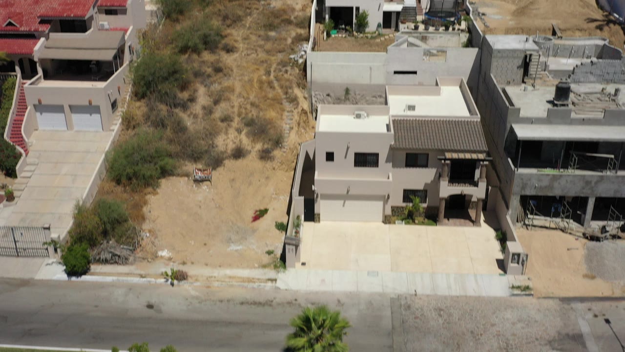 Aerial view of modern hillside homes beside dry scrub terrain.