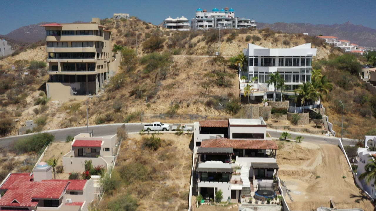 Hillside modern buildings above a curving road under blue sky.