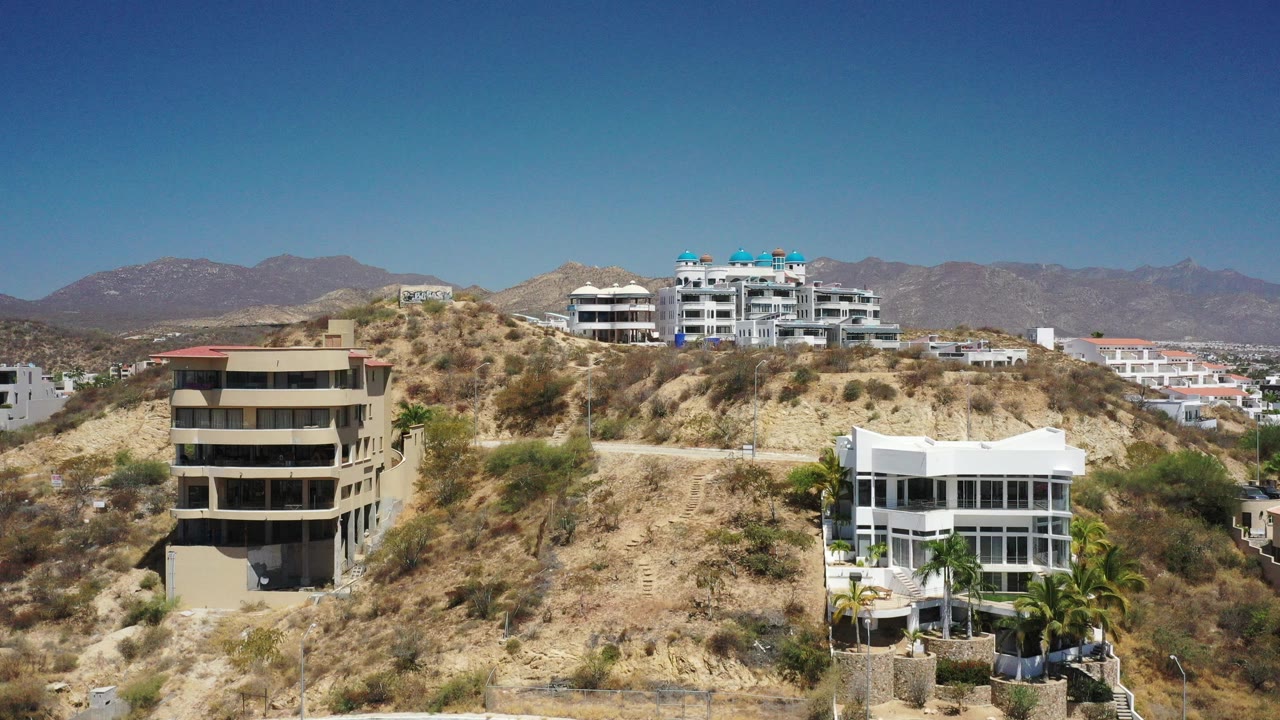 Hillside buildings with dry brush and distant mountains under blue sky