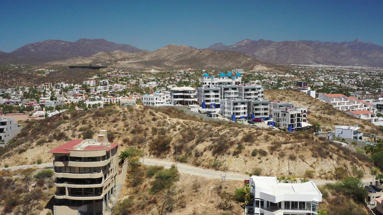 Drone view over dry hills, residential buildings, and distant mountains.