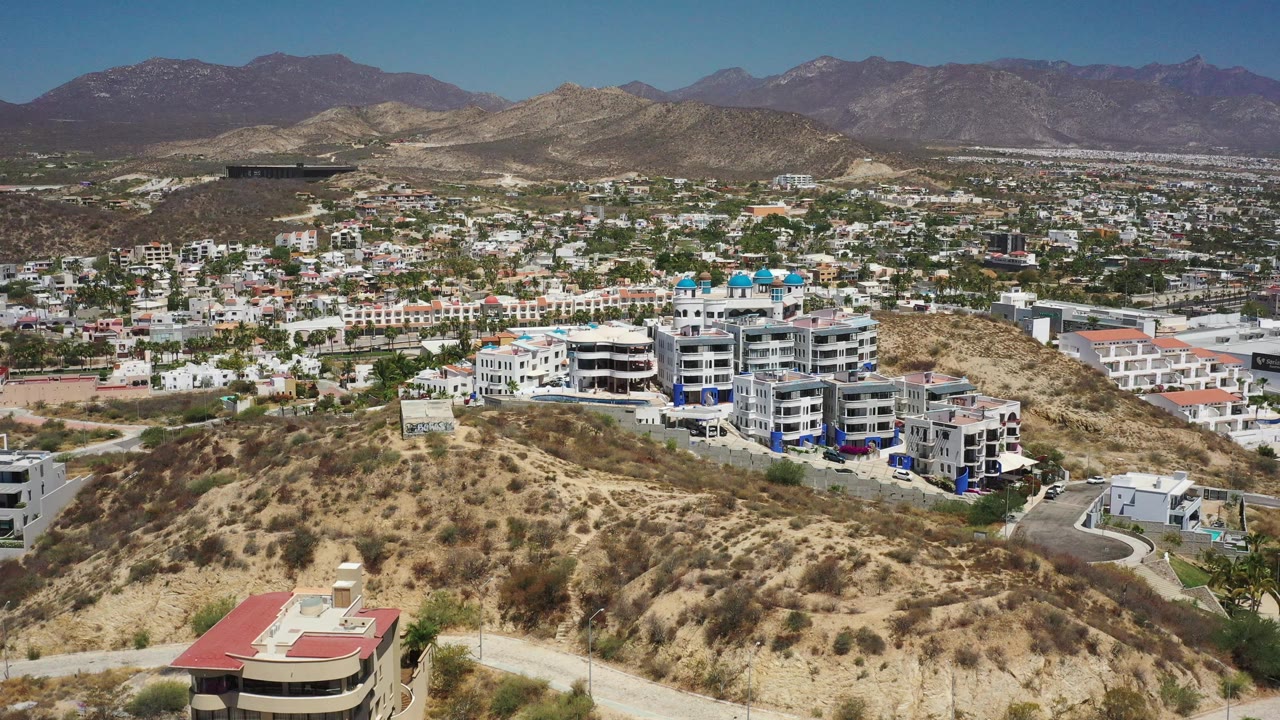 Wide aerial over hillside residences with pools and distant mountains.