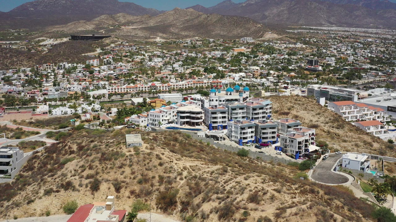 Aerial view of arid hillside apartments and a city below mountains.