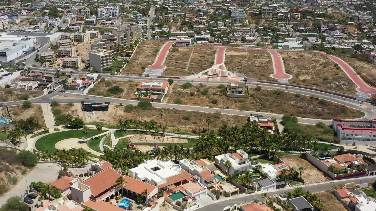 San Jose del Cabo aerial view with red-paved access roads across dry land, residential roofs and pools in the foreground, and no visible people.