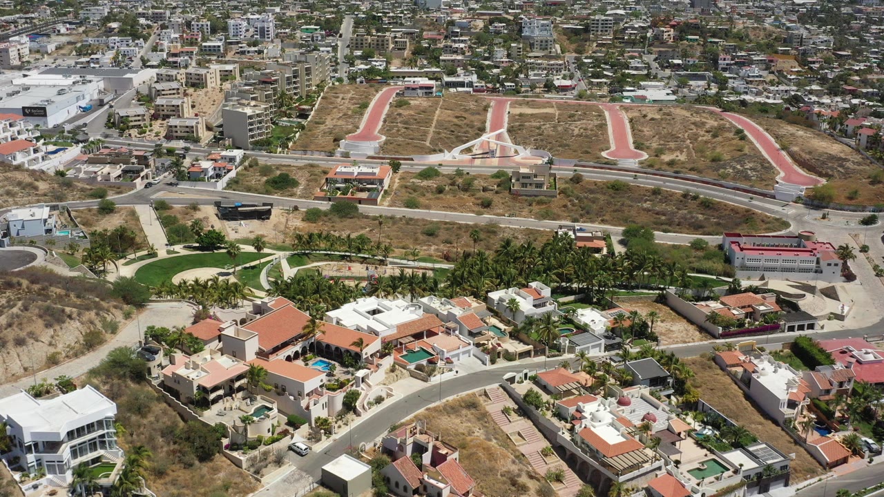 Aerial view over hillside homes, roads, and a low-rise city background.