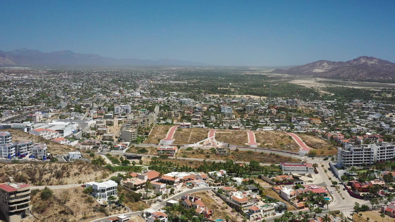 San Jose del Cabo fills the frame from foreground homes and hillside streets to a broad low-rise city grid and hazy mountain horizon, with no visible people.