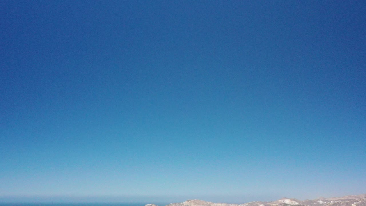 Blue sky over distant ocean and low coastal hills.