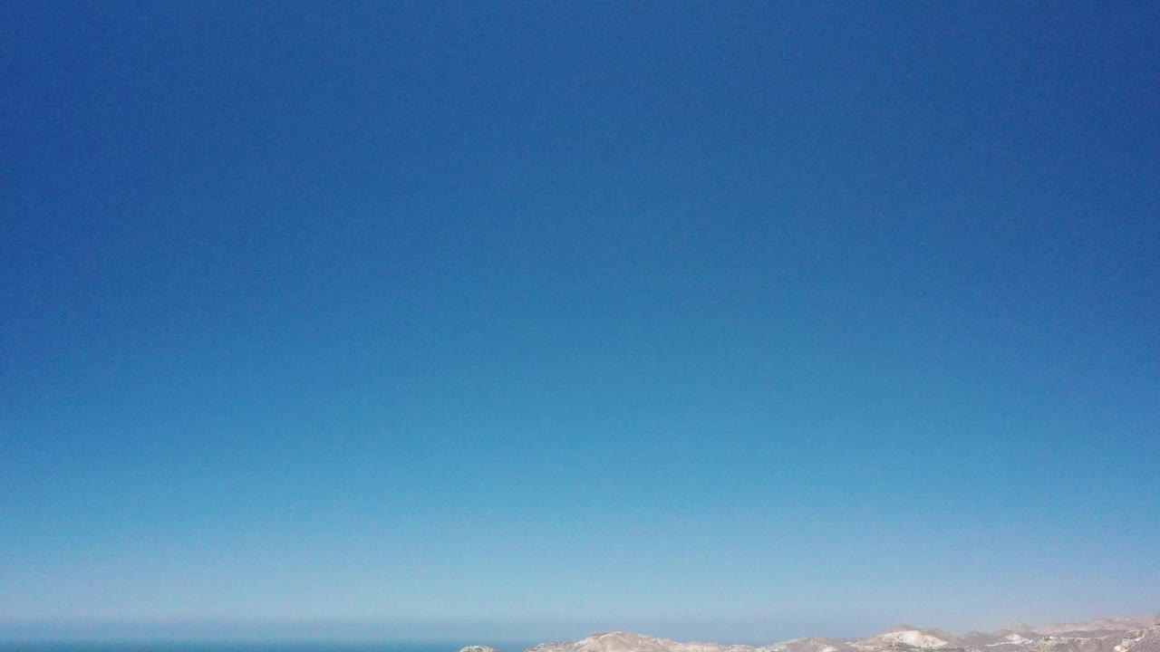 Aerial frame over San Jose del Cabo showing a large clear sky, blue ocean band, faint distant landforms, and no visible people.