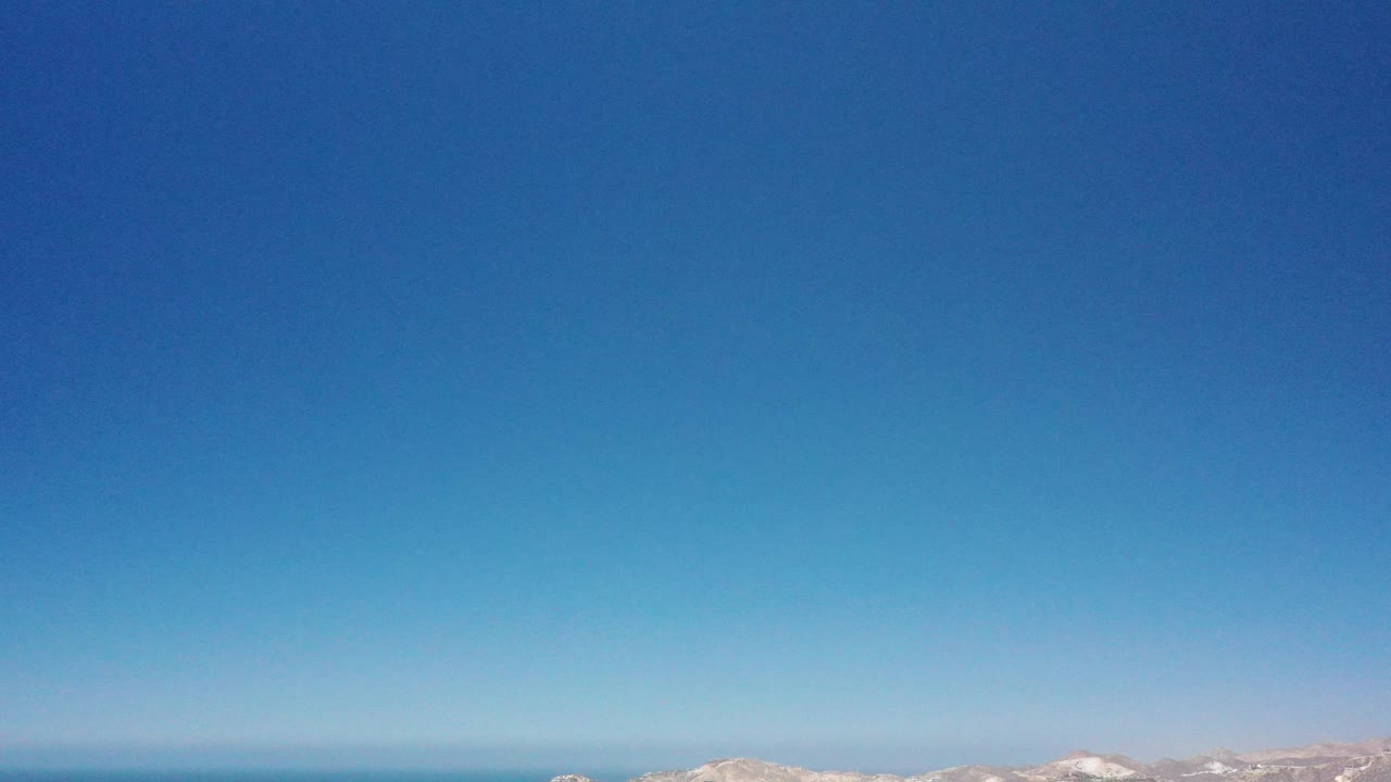 Blurred aerial moment in San Jose del Cabo with turquoise water, pale surf, vertical streaking, and no visible people.
