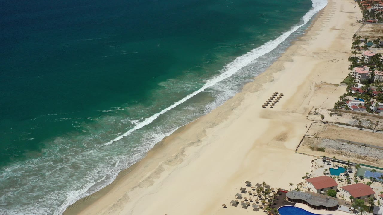 Aerial view of blue-green ocean beside a wide sandy beach.