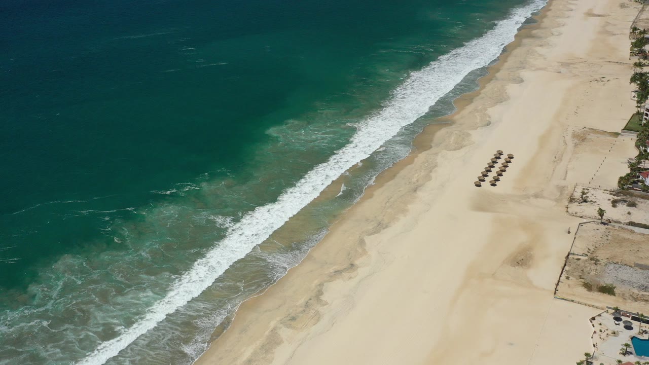 Aerial view of teal ocean surf breaking onto a sandy beach.