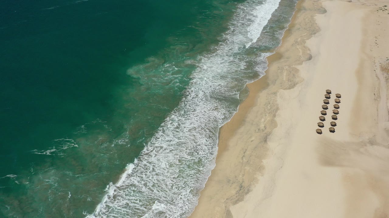 Aerial view of turquoise ocean meeting pale sand with rows of beach umbrellas.