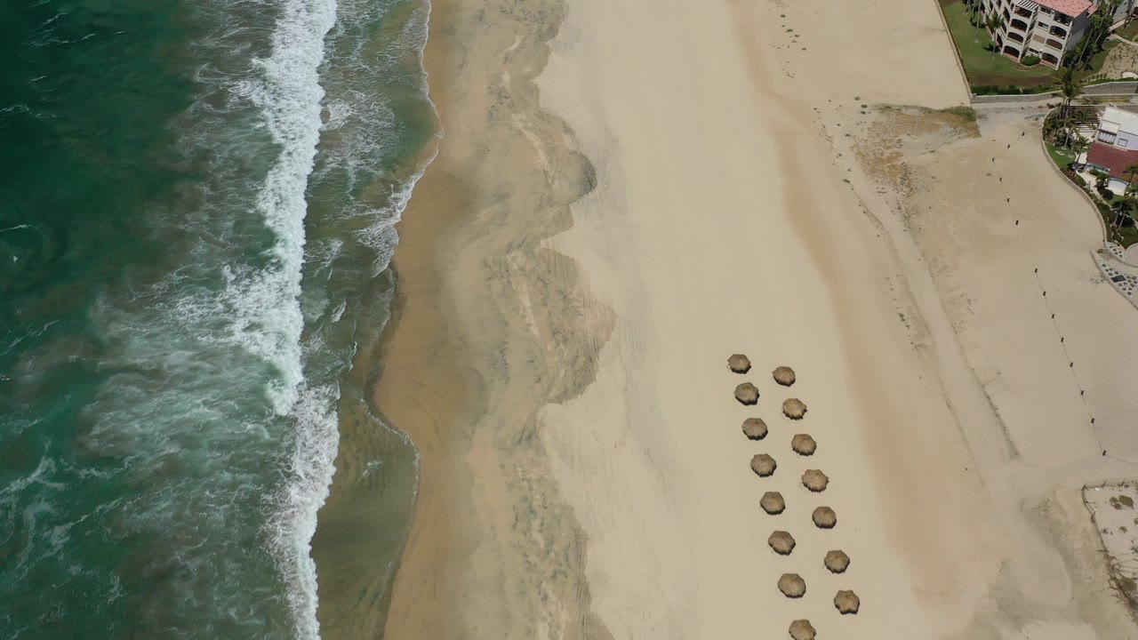Aerial view of surf, sandy beach, umbrellas, and beachfront buildings.