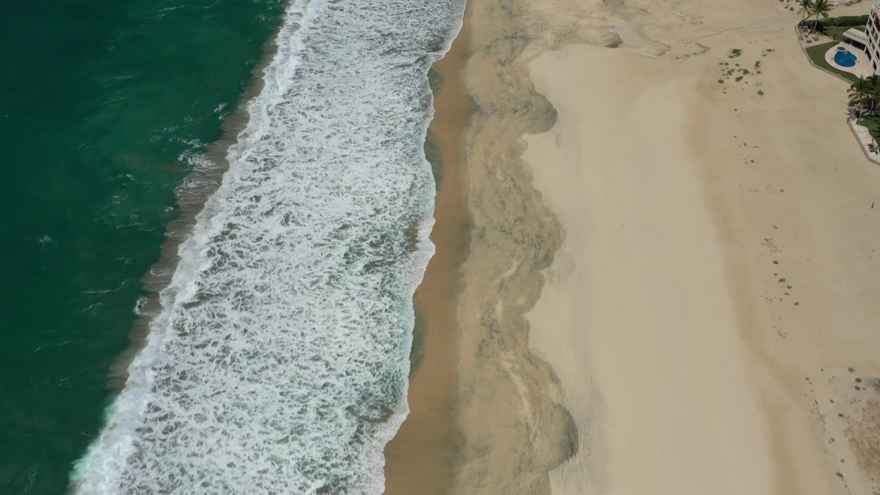 Aerial view of green ocean waves breaking onto pale sand.