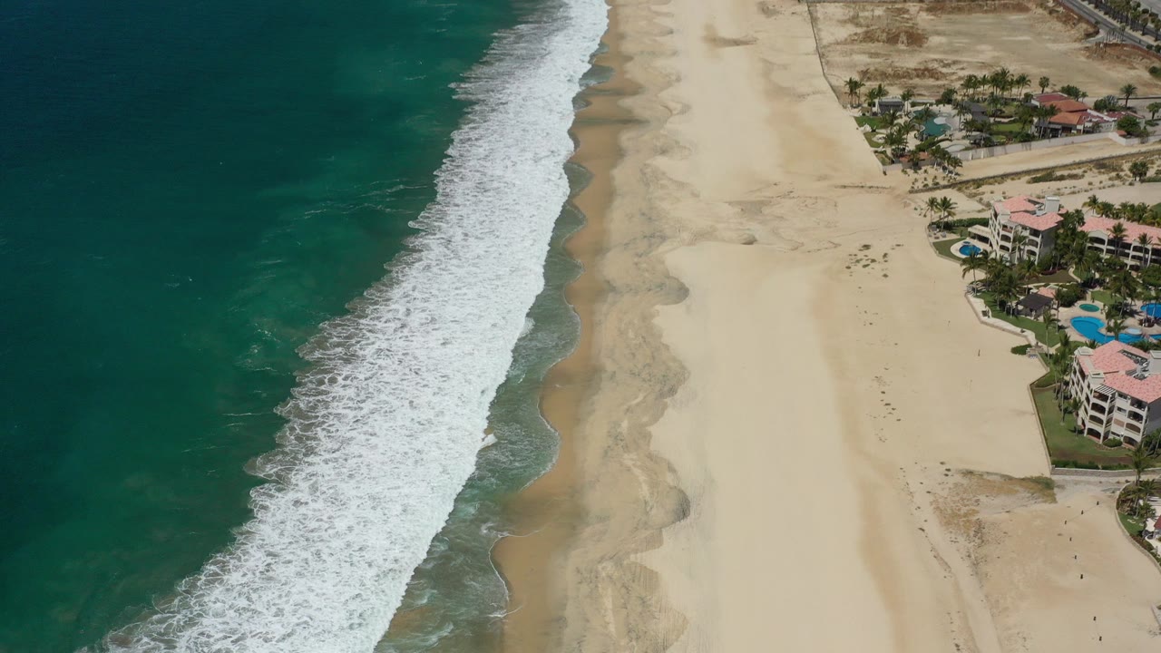 Aerial view of blue-green ocean surf beside a wide sandy beach and beachfront buildings.