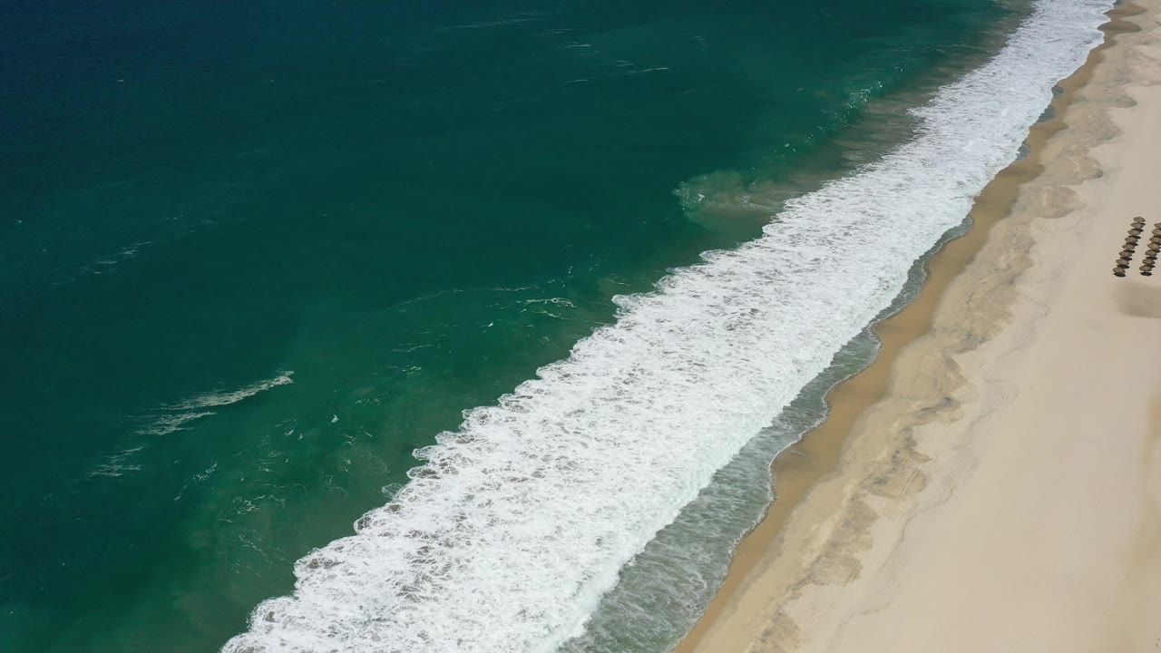 Foamy shoreline curves beside deep blue-green water