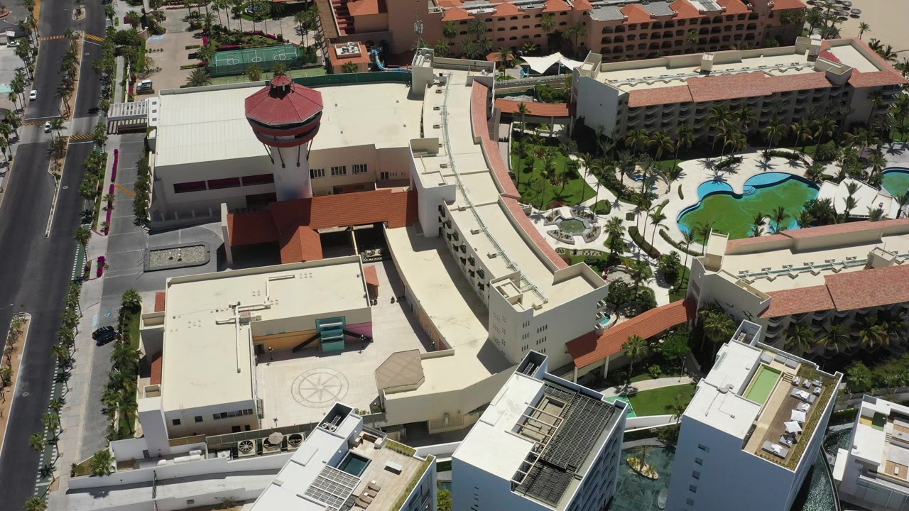 Drone view of resort rooftops, red circular tower, pools, and street.