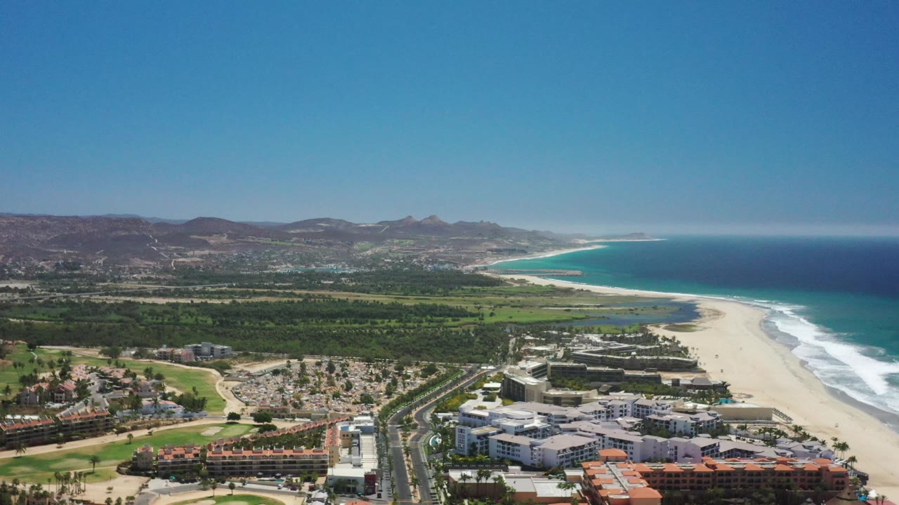 Beach town below hills beside a long sandy shoreline and blue sea.