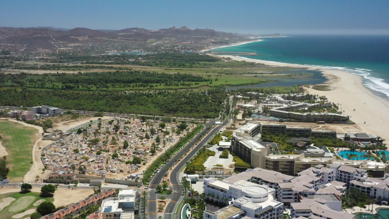 Aerial view of coastal buildings, road, beach, ocean, and hills.