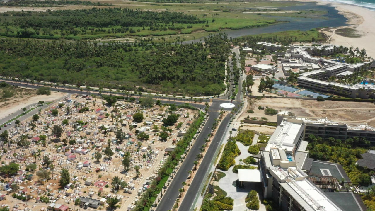 Aerial view of a road, buildings, dirt lot, trees, and coastline.