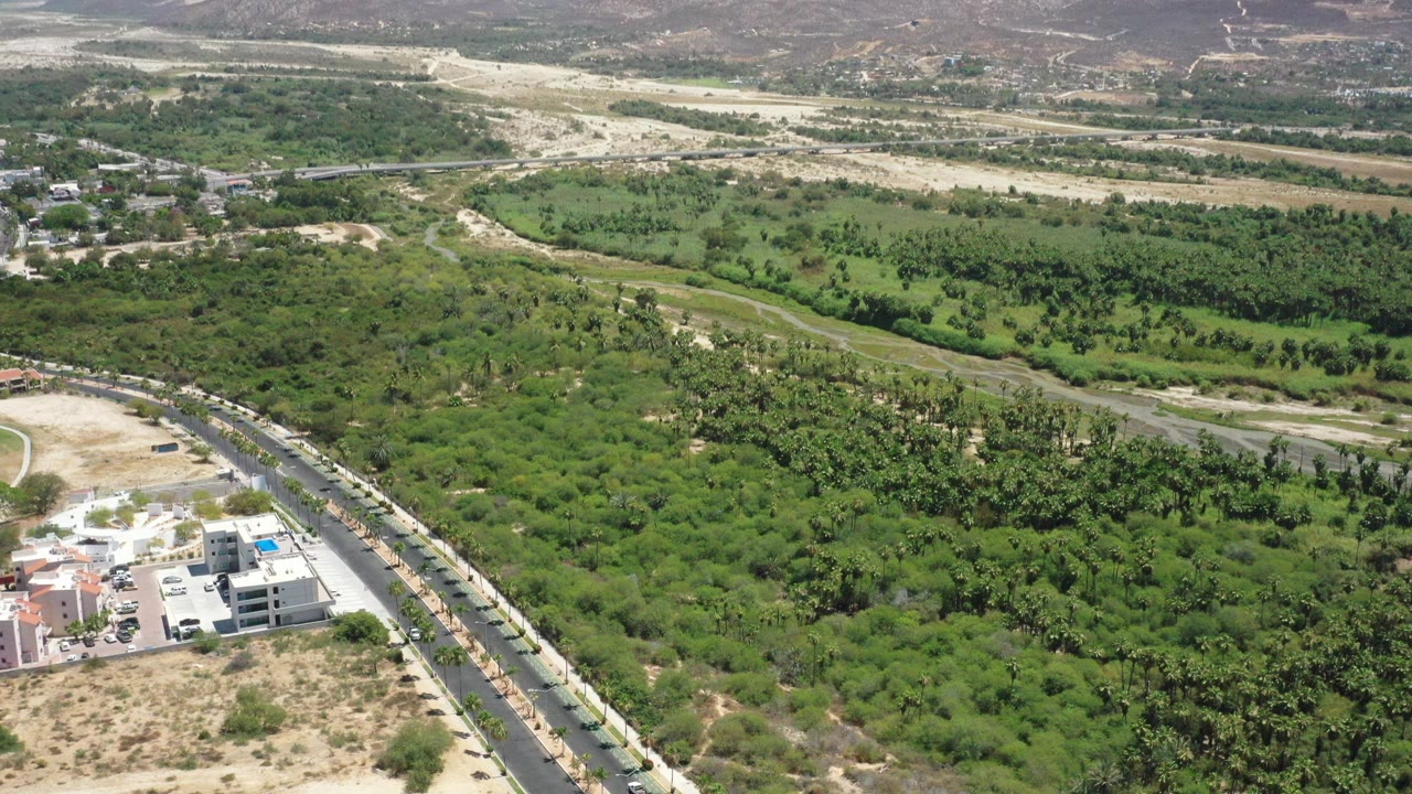 Aerial view of green vegetation, road, buildings, dry washes, and mountains.