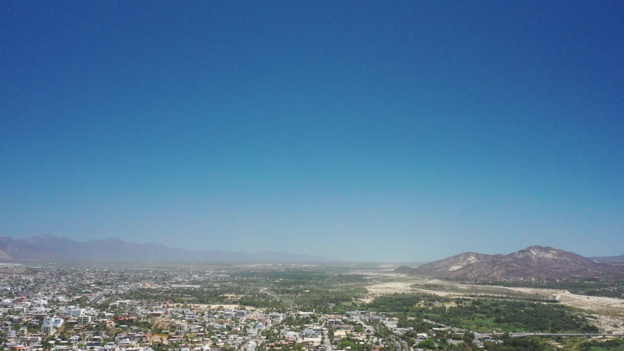 Wide aerial view of city, green terrain, dry hills, and blue sky.