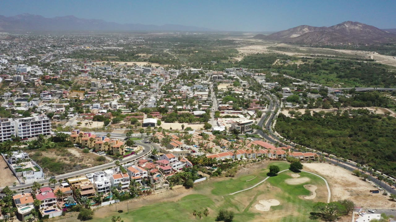High aerial view of city streets, homes, golf course, trees, and distant mountains.