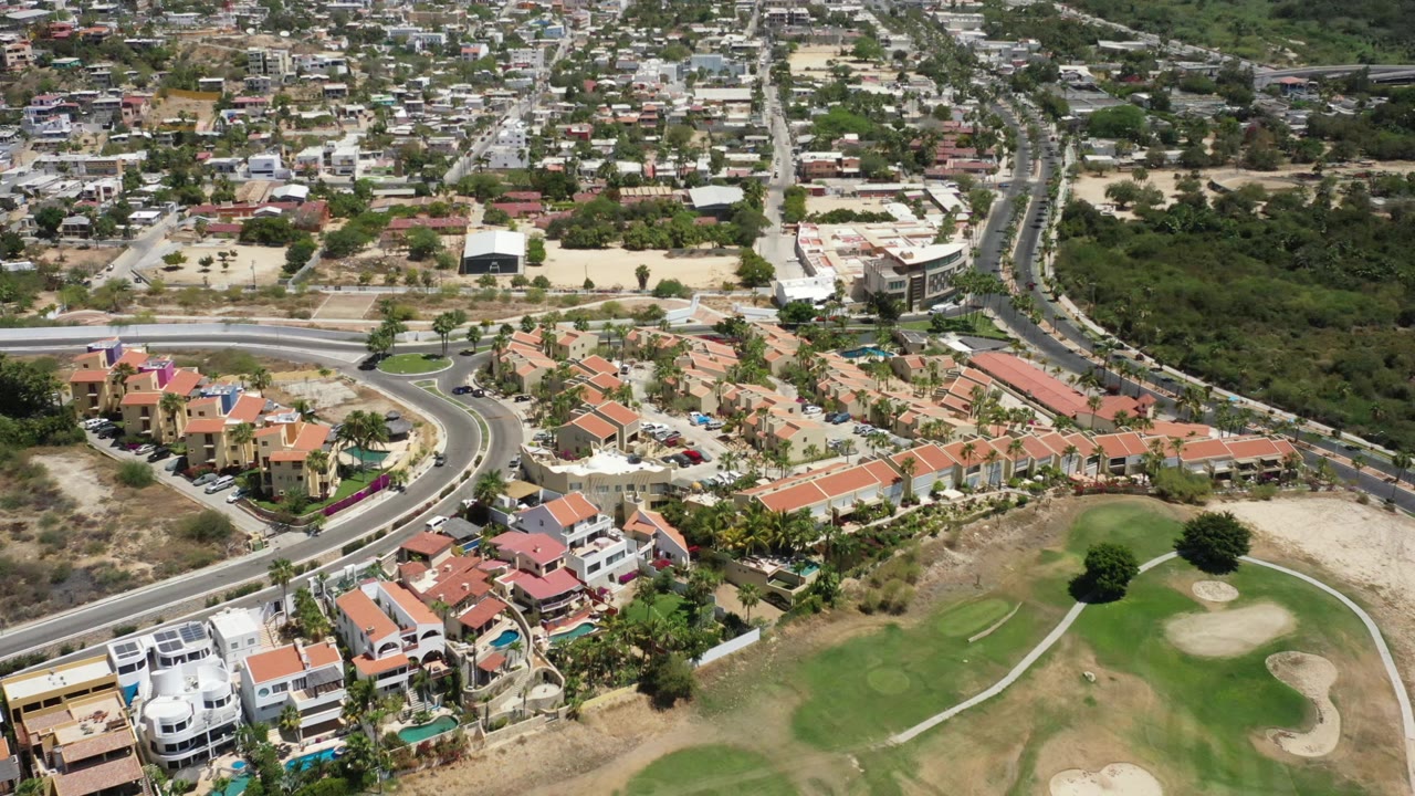 San Jose del Cabo aerial view showing clustered tile-roof houses, landscaped yards, a sweeping road, golf greens, bunkers, and no visible people.