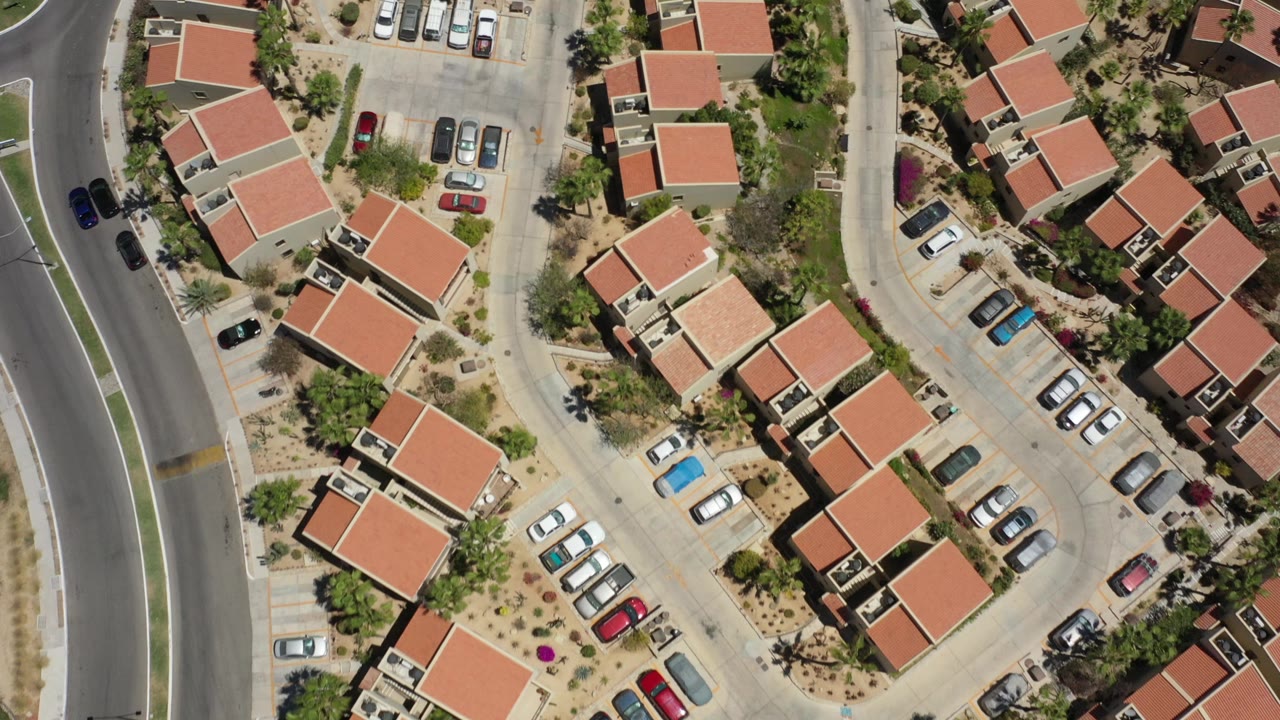 Top-down frame of San Jose del Cabo residential buildings, red tile roofs, a central parking court, and a broad curved road at the edge, with no visible people discernible.