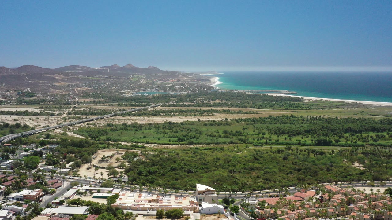 Wide aerial view of coastal town, green valley, mountains, and blue ocean
