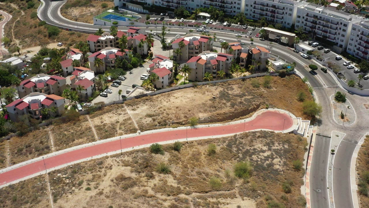 Aerial view of apartment buildings, curving roads, dry lots, and a red path.