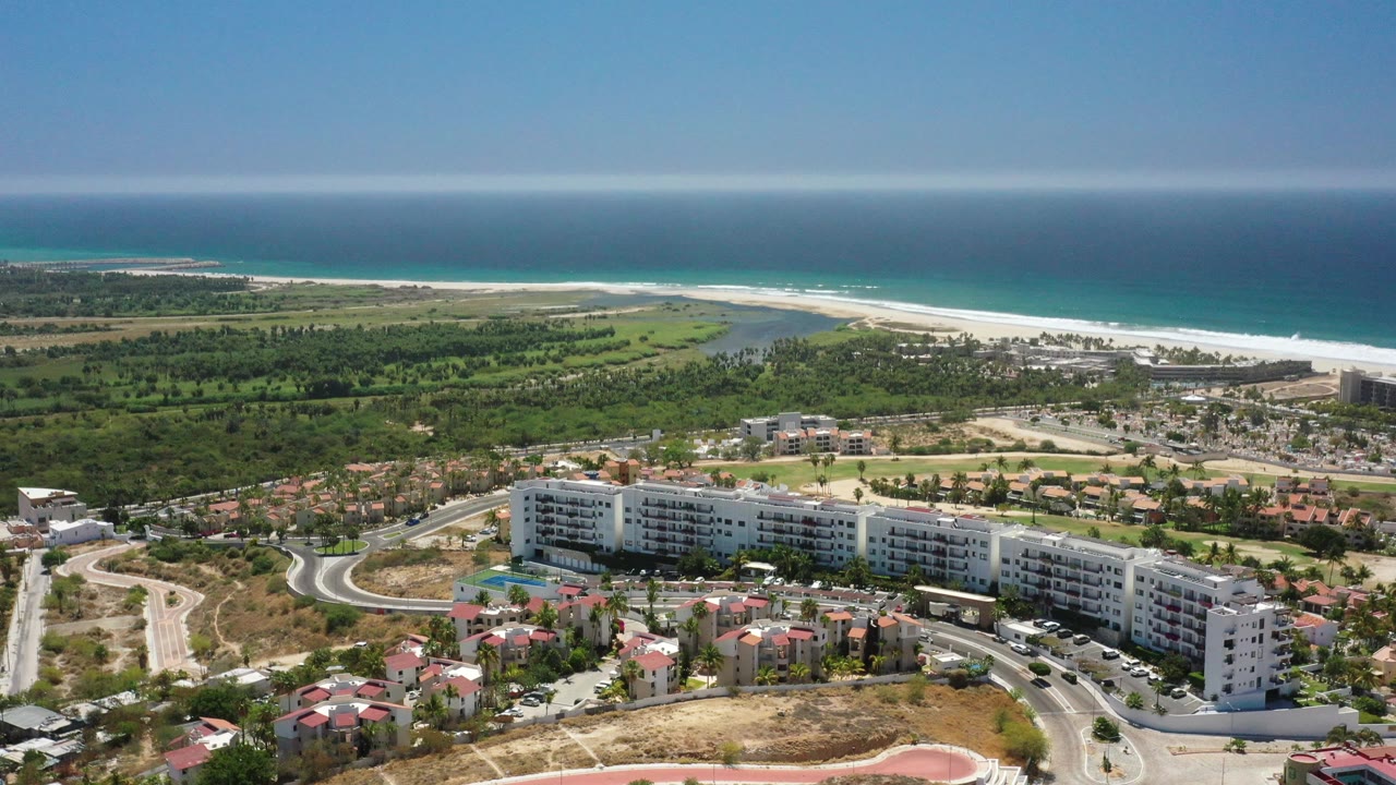 Aerial coastline with curved road, beachfront buildings, beach, and blue ocean.