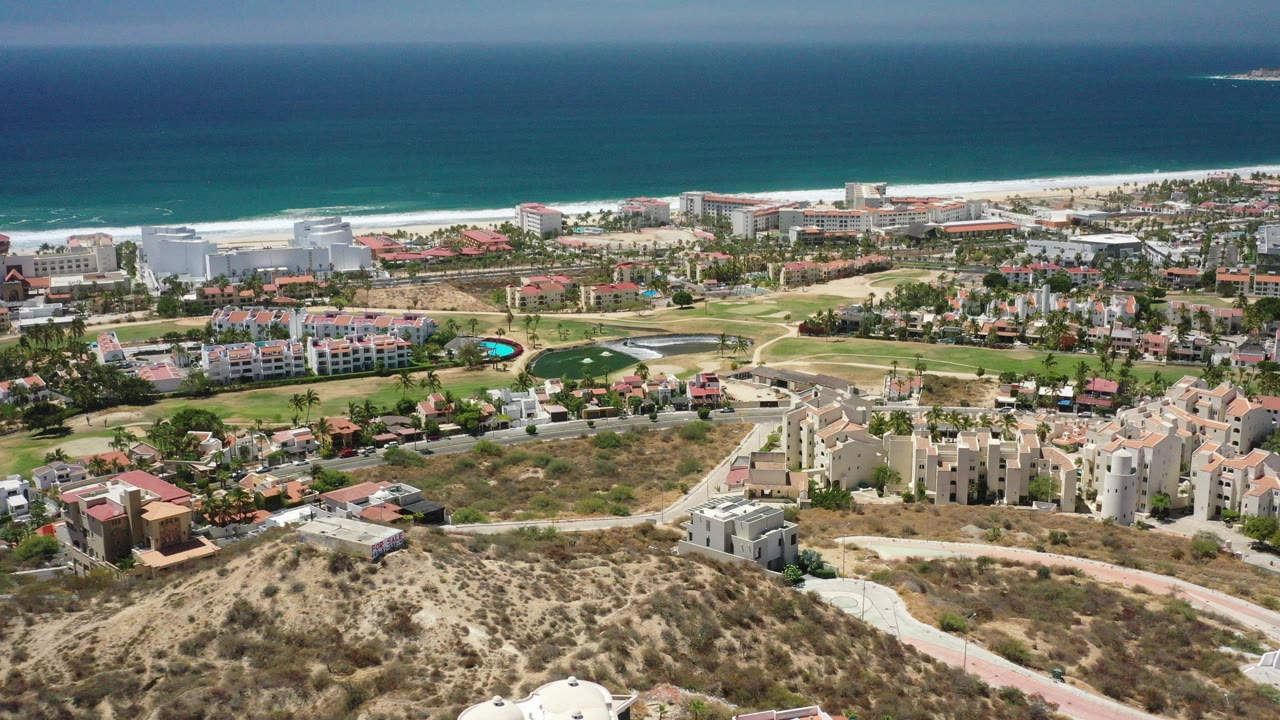 Aerial view of coastal villas, golf greens, beach, and blue ocean.