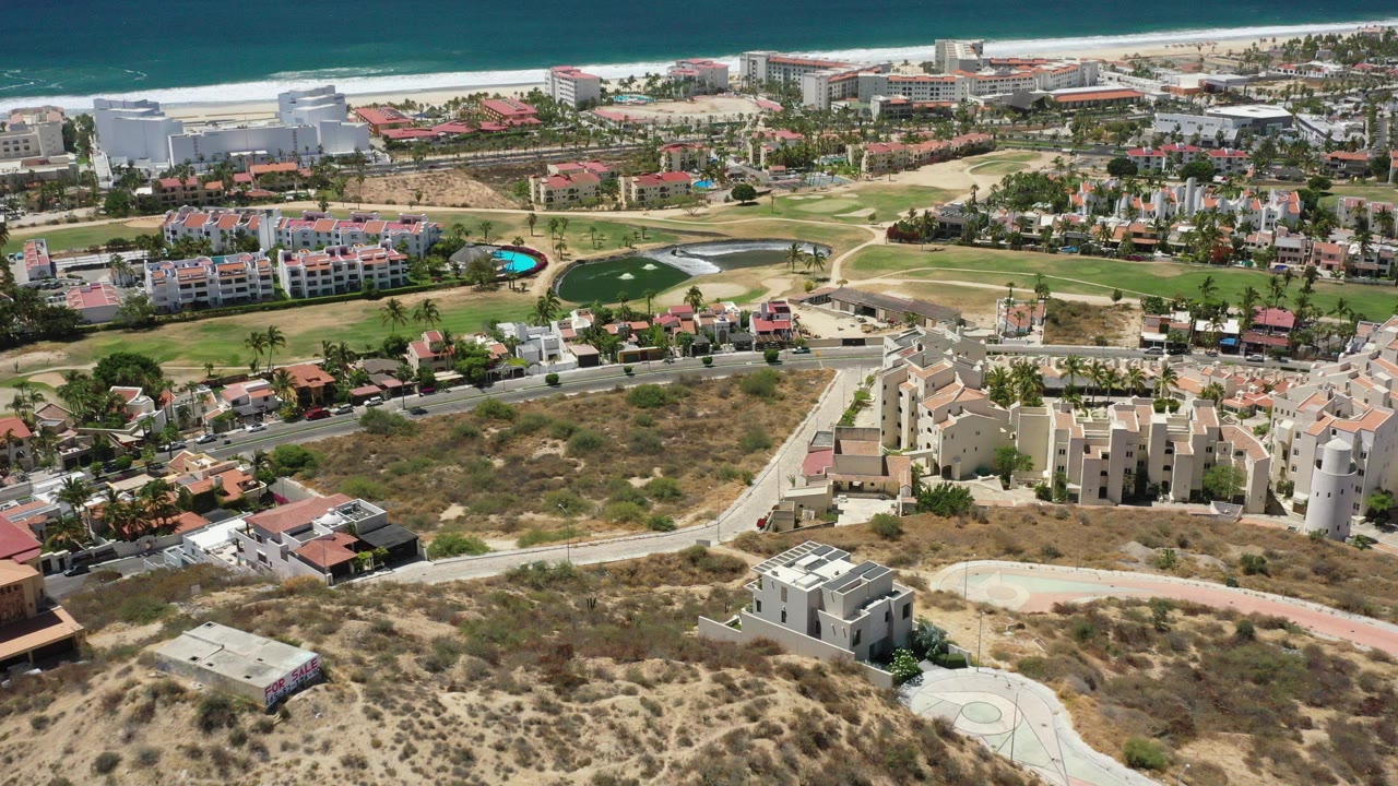 Aerial view of coastal neighborhood, dry lots, roads, homes, and ocean beyond.