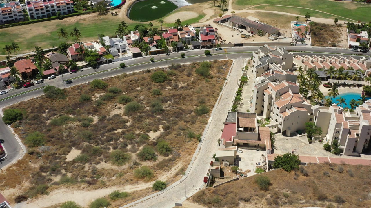 Overhead view of resort homes beside dry scrubland and a curved road.