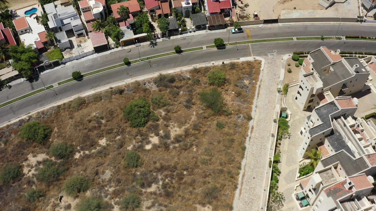Aerial view of modern homes, a curving road, and a dry vacant lot.