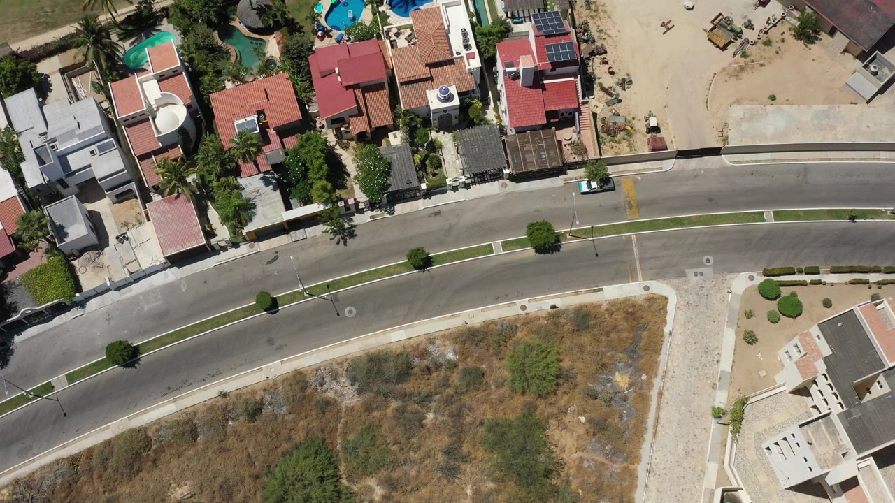 Top-down aerial view of private homes beside a curved road and dry lot.