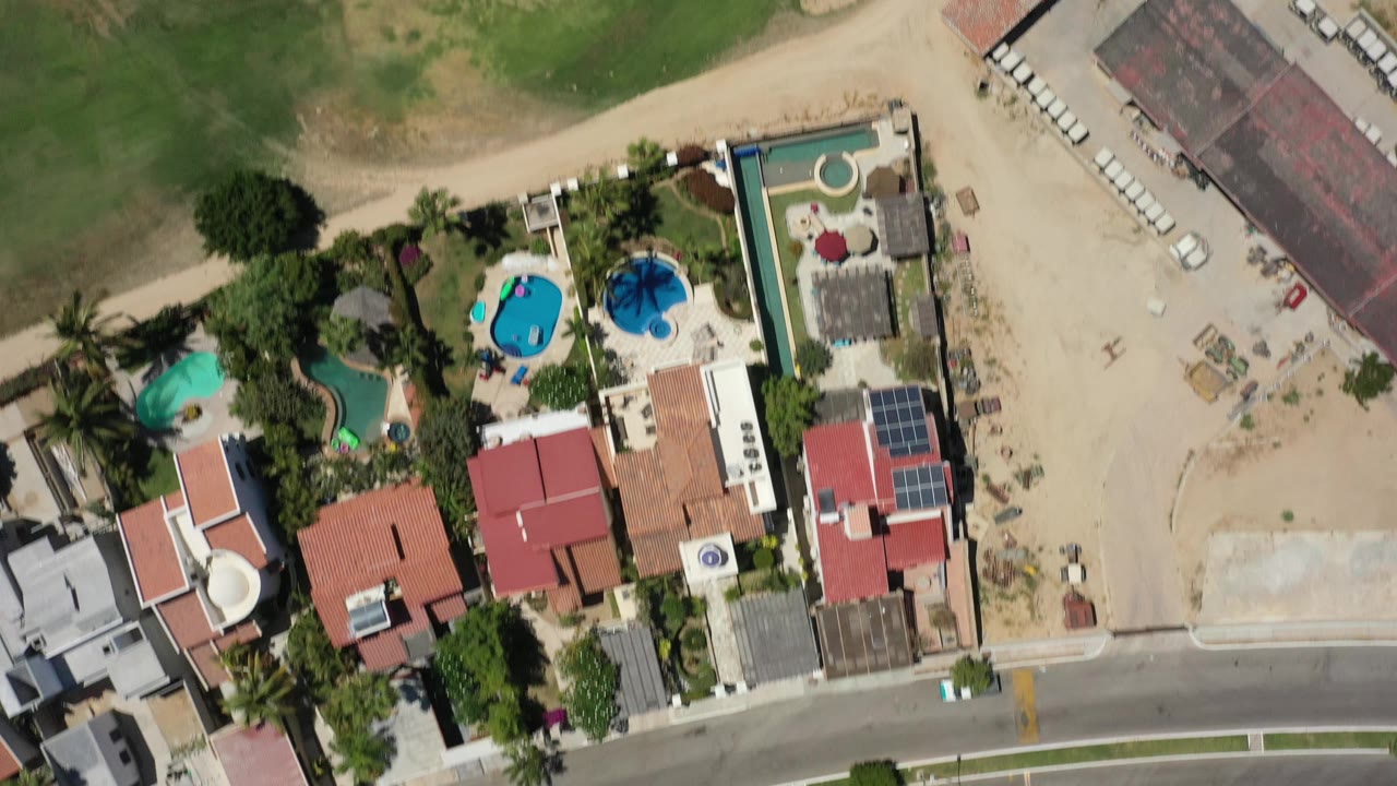 Top-down aerial frame of homes beside a road and golf course edge.