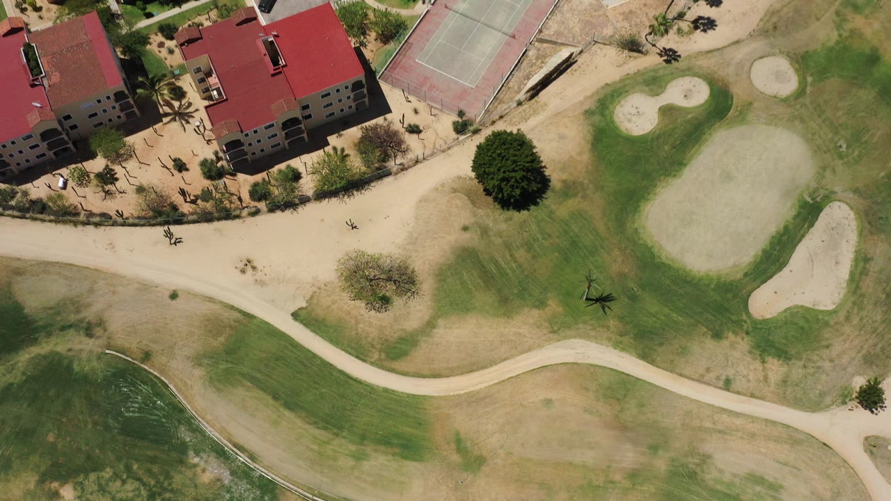 Overhead view of red-roof buildings beside golf greens and sand traps.