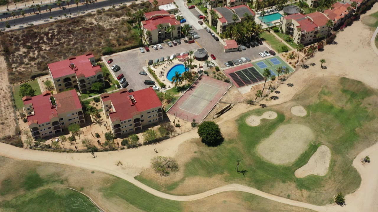 Aerial view of red-roof resort buildings beside golf greens and sandy paths.
