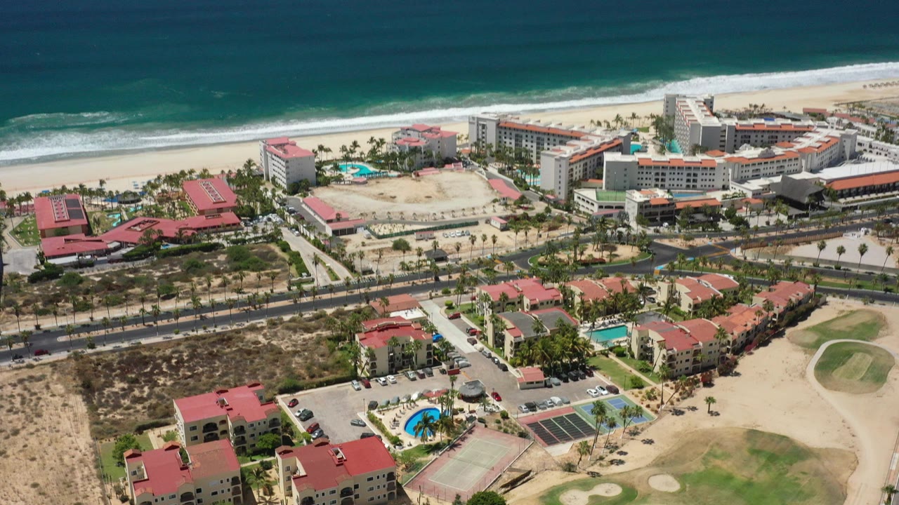 Aerial view of beachfront resorts, villas, pools, sand, and blue ocean.