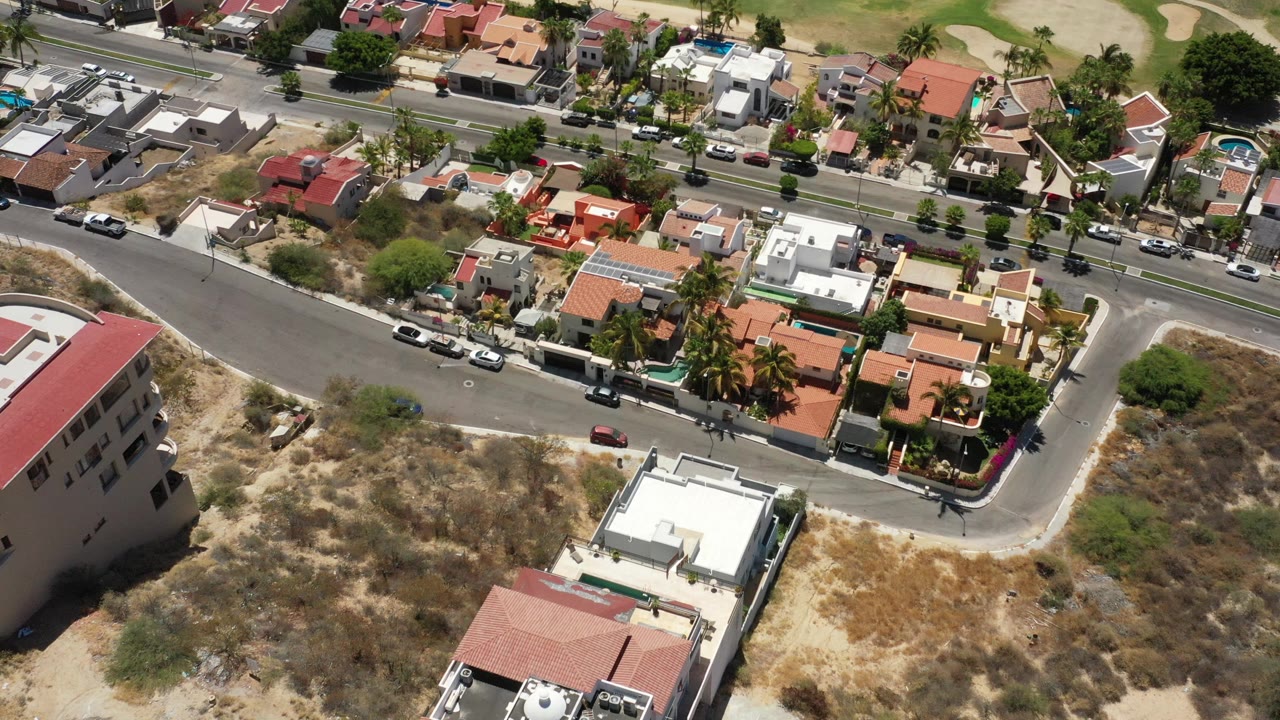 Drone-style view of a residential block with cars and green space beyond.