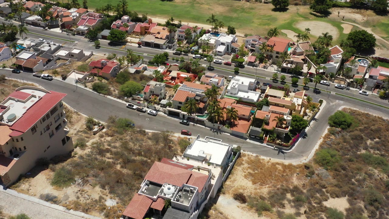 Aerial view of hillside homes, roads, dry lots, and green land beyond.