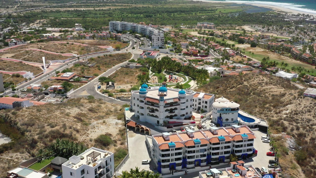 Aerial view of a white building with blue domes near roads and dry hills.