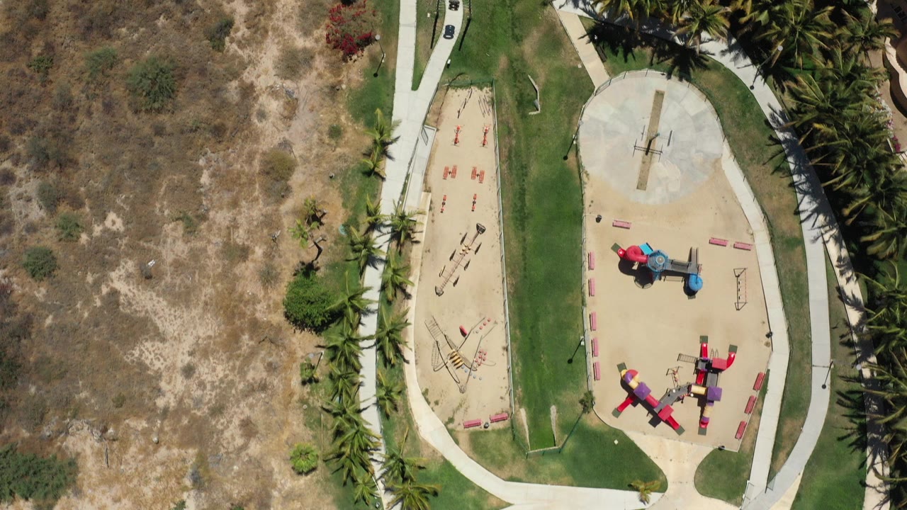 Overhead view of a playground beside grass, dirt, palms, and paths.