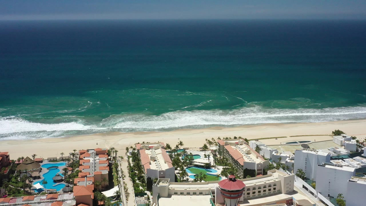 Beachfront resort area below a band of ocean and white surf.