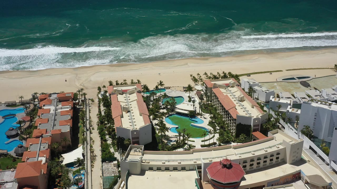 Beachfront hotel complex with pools and palms below ocean surf.