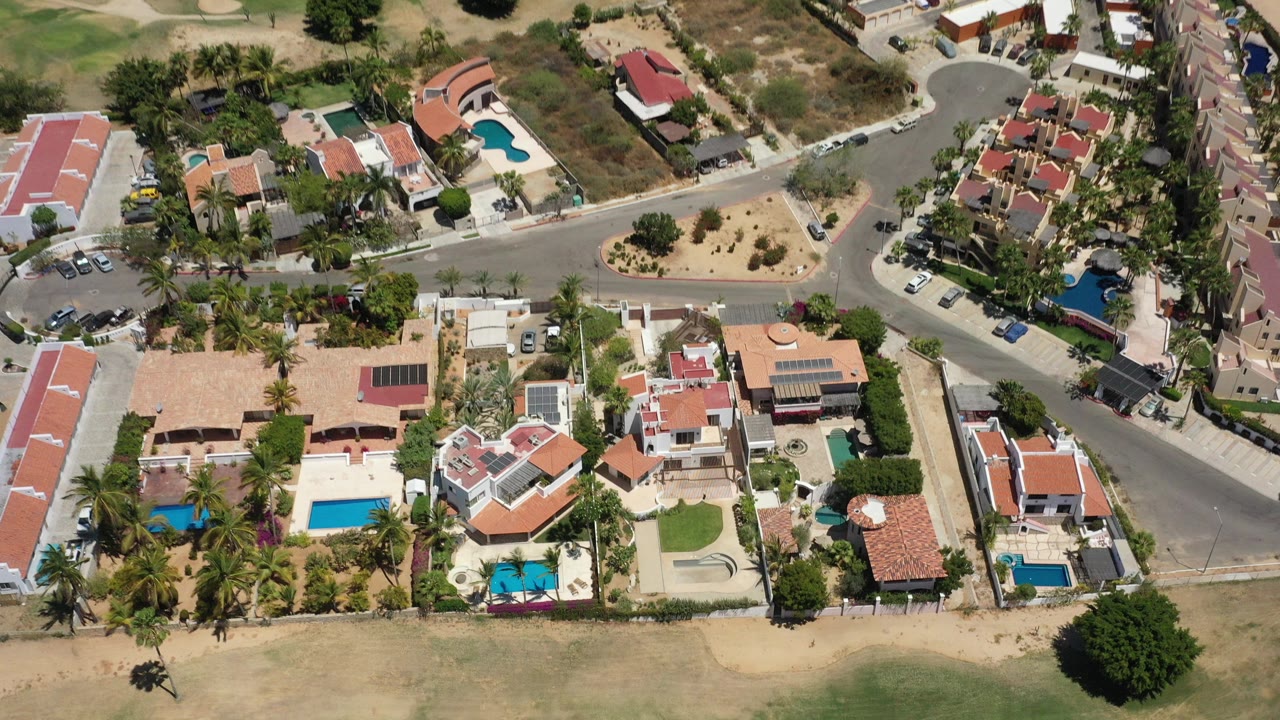 Overhead view of homes, pools, roads, palms, and dry lots.